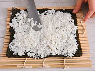 3、寿司,取一片紫菜放寿司帘上，将米饭均匀抹一层在紫菜上。