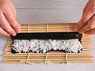 6、寿司,卷起寿司帘带动紫菜卷起来。一定要卷紧。