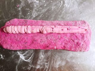 9、火之舞（火龙果）奶酪软欧包,醒发好的面团用手轻拍排气，将光面向下，在面饼上方挤上一条奶酪馅，从上至下将奶酪包紧后，搓成长条状