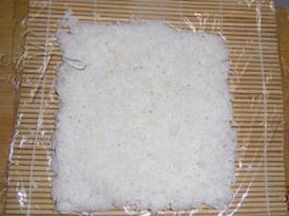 3、黄袍加身寿司,将一碗米饭倒入翻拌均匀，铺在放了一层保鲜膜的寿司帘上