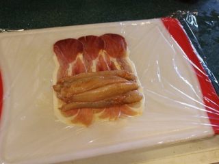 4、 鮟鱇鱼生火腿佐芒果酱汁,铺一张保鲜膜，摆上生火腿片。将鱼肉摆上。