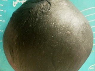 6、竹炭粉黑芝麻花朵面包,拿出来排气,滚圆(面团表面有小气孔,说明面团揉到位了),用保鲜膜盖起来,醒发十五分钟左右