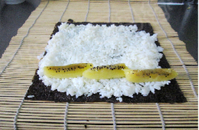 3、金艳果沙拉寿司,将一段放上金艳果猕猴桃条，用寿司帘辅助一点一旦卷起来