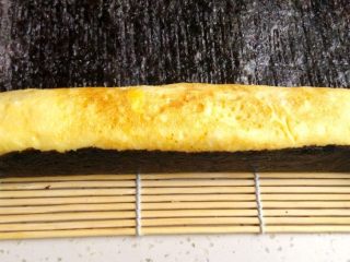 7、紫菜蛋包饭,将做好的鸡蛋卷取出，放在烤紫菜片上，用寿司卷帘辅助，小心卷起