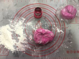 4、自制火龙果面,案板上洒写干粉,把面团分成2份,一份用保鲜袋装着