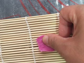 10、自制火龙果面,把面皮放在寿司席上,用大拇指往前一推,就好了