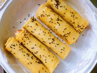 6、酸黄瓜吐司卷,将包好的吐司卷,在鸡蛋液中来回滚,待均匀的沾满鸡蛋液后,撒上些许黑芝麻。