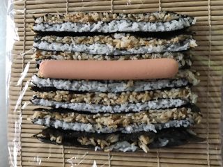 6、木鱼花香松花朵寿司,寿司帘铺保鲜膜，然后把切好的寿司条竖着按咖啡色白色的顺序摆好。中间摆上火腿肠。
