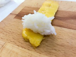 4、宝宝辅食:宝宝芒果饭-12M+ ,取一片芒果,捏一小团米饭,直接用手卷起即可,卷一圈多一点就可以啦,可以在芒果下面垫一层保鲜膜,会更加好卷。