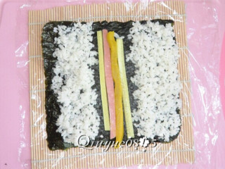 7、翻转樱花寿司,然后再在海苔的两侧放一些米饭，不要太厚了。中间放上火腿肠、黄瓜、大根条（如图）