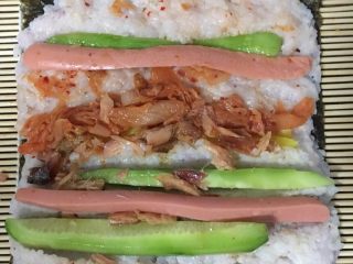 3、青瓜火腿腊鱼寿司,米饭晾冷后，铺在海苔上面！米饭太热，会把海苔烫软，卷不起来！所以一定要晾冷才能铺！米饭铺好后，就放配料～想吃什么放什么～????