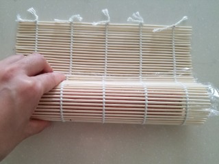 11、樱花寿司,拖动保鲜膜使海苔置于竹帘的边缘处,然后对折成水滴状,用两手用力压紧。