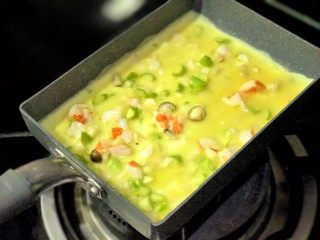 8、幸福满满厚蛋烧(宝宝辅食),然后将都是料的那碗蛋液下锅,前后左右摇匀,让蛋液和食材均匀分部在锅底。