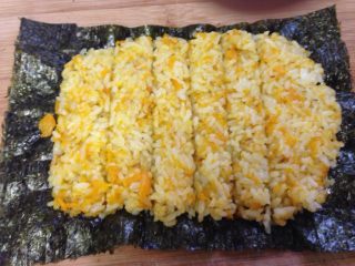 4、南瓜寿司,取一片紫菜，把南瓜饭铺上去，用勺子摊匀。