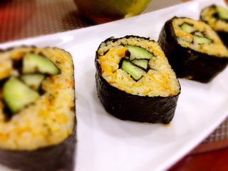5、南瓜寿司,中间摆上黄瓜条，用竹帘卷起紫菜卷，刀身沾点寿司醋，把紫菜卷横切成块，摆盘。