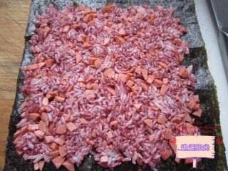 6、花朵????寿司????,将另一份加入火腿粒，并撒入少量的红曲粉搅拌均匀，取一张紫菜，均匀的铺在上面