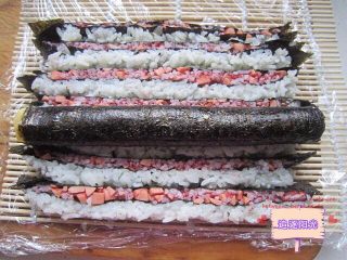 9、花朵????寿司????,寿司帘用保鲜膜包好。将切好的寿司条竖起按照红白相间的顺序放到寿司帘上，中间放上卷了紫菜的蛋卷