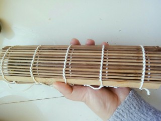 4、寿司,然后开始从下往上卷，卷的时候注意不要把帘子卷进了饭里哦，要一边卷，一边往上拉竹帘，卷好后用力握几下，固定下形状，防止切的时候变形散掉！(因为一个人做，不方便拍这部，大家做的时候注意下就可以)