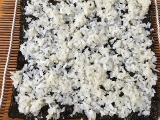 3、寿司,把海苔放在竹帘上，将糯米均匀的铺在海苔上（这里我没有放寿司醋，因为孩子不喜欢）
