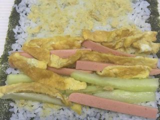 3、简易寿司,把肉松、黄瓜条、火腿条、鸡蛋条铺在米饭上。