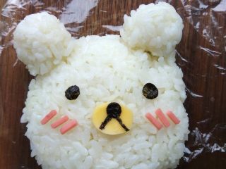 5、小熊米汉堡,将少许米饭放在保鲜膜中，团出两只耳朵。并用奶酪片和寿司紫菜，刻出五官。放在一边备用。