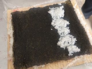 5、翻转樱花寿司,在把紫菜翻过来，撒有樱花粉米饭朝下，光滑紫菜面朝上，在靠自己方向三分之一处铺一些米饭