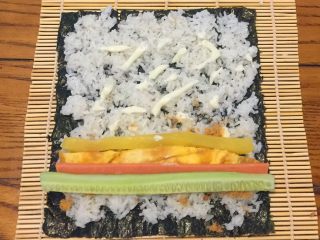 4、超简单寿司做法,把黄瓜，火腿肠，鸡蛋，调味萝卜平铺在肉松上，从自己这边往外卷