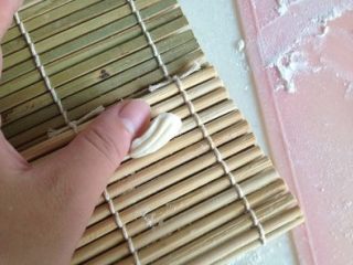 4、炒猫耳疙瘩 ,借用寿司帘额纹理,放一个小面剂子,用大拇指由下至上轻搓!(如果没有寿司帘,直接在案板上搓也成)。