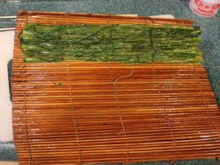 4、清烫空心菜佐黑芝麻酱,将烫好的空心菜头尾两边平均交迭，放置在寿司的竹卷上。