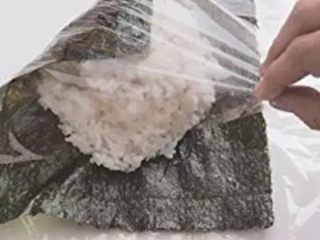 6、饭团便当,借保鲜膜把海苔的一个角拉过来,对角线的另个角也拉过来包好。同理再把另外两个角也包进来,用保险膜裹紧。