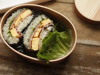 7、饭团便当,把包好的饭团切成两半,放进便当盒。中间用生菜叶子隔开,右边空档的地方可以放自己喜欢的水果啊,蔬菜啊之类的。