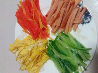 2、五彩寿司,胡萝卜，黄瓜，火腿肠，摊好的鸡蛋饼，都分别切成丝摆好，热水焯下胡萝卜，黄瓜丝。