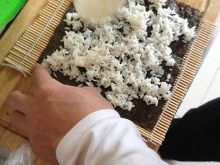 3、爱心❤️寿司,隔夜的米饭蒸好，放的不太热，取海苔皮一张铺到卷帘席上，把米饭铺好。