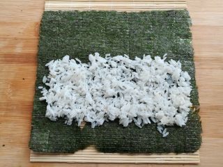 6、金顶寿司,在寿司帘上放上大片的紫菜，铺上一部分的米饭，前段留一半，末端留一小节不铺米饭