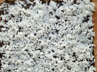 4、培根寿司卷,把米饭均匀展开，尽量薄，因为太多吃两个就饱了。注意四边要铺上米饭不能空。