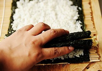 11、小花寿司,先在步骤10的白米饭的一端放两瓣花瓣寿司，然后在这两瓣花瓣的中上方放上花蕊，最后再将花蕊两旁放上两瓣花瓣，最顶部放上一瓣花瓣，用手扶住；