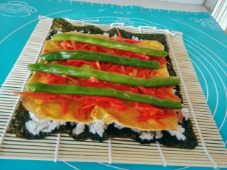 14、金枪鱼饭卷,将胡萝卜丝，铺在鸡蛋饼上，摆上四根四季豆。