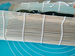 18、金枪鱼饭卷,借助寿司帘，将紫菜卷慢慢卷起来，尽量卷紧一点。