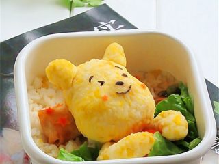 9、维尼熊便当,另取一个便当盒,先铺上米饭,春卷做枕头,生菜下面可以塞一些自己喜欢吃的菜,维尼怀里抱了一个小西红柿,然后捏两个米饭条做维尼的膀子,维尼枕枕头