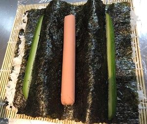 2、花朵寿司,中间的位置放上火腿，两侧摆上黄瓜条。火腿肠用细的，黄瓜条也务必切细一些哦，然后黄瓜条切成三角状，尖的那头尽量往下摆放，这样切出来才好看。