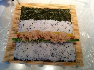 4、紫菜包饭,将刚刚准备好的黄瓜条、腌萝卜条、火腿肠条和肉松放到米饭的中间位置。