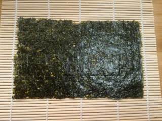 6、紫薯寿司,取半张海苔铺在卷帘上。今天的这种卷法只需要一次半张就够了。做寿司的紫菜是专门的寿司海苔,不是普通的紫菜哦,超市有售。
