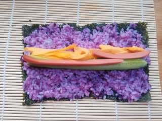 8、紫薯寿司,把拌匀的紫薯米饭均匀的铺在紫菜上,紫菜的两端也要有米饭粒。如果觉得米饭比较粘,可以用勺子沾水,有勺背来把米饭推均匀。用手来操作的话,也可以在手上抹些凉开水,或寿司醋防止黏手。