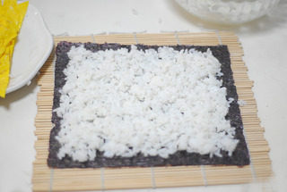 4、爽食寿司卷,在寿司帘上放上寿司紫菜,将米饭铺平,不要压饭粒,尽量保持饭粒完整,松软,四周稍微留一点边。