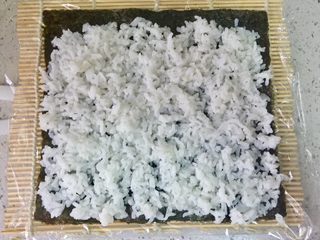 3、牛油果肉松寿司,把寿司海苔铺在寿司席上，铺上一层米饭，留出一条边。