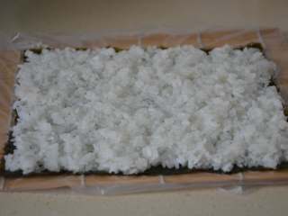 12、寿司,用手将米饭均匀的平铺在海苔上。用手轻轻压实，将四周多余的米饭摘干净。