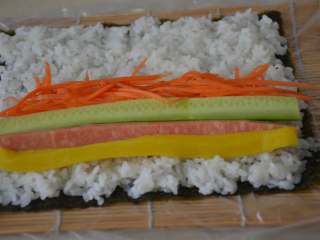 13、寿司,在靠近自己的一边，依次摆上寿司大根条，黄瓜和火腿条。放适量的胡萝卜丝。