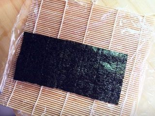 5、樱花寿司,首先将寿司帘上铺上保鲜膜，再放上一片海苔。