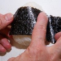 3、蜜汁小卷三角饭团,取1张海苔切成宽5公分的长条状，去除包覆饭团的保鲜膜，将海苔条包裹一圈在饭团外，最后在饭团上撒些香鬆增添风味即可。