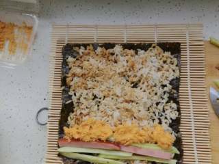 3、寿司,木帘上先放一张海苔，再铺好办好的米饭，放上黄瓜条，火腿条，牛肉松。